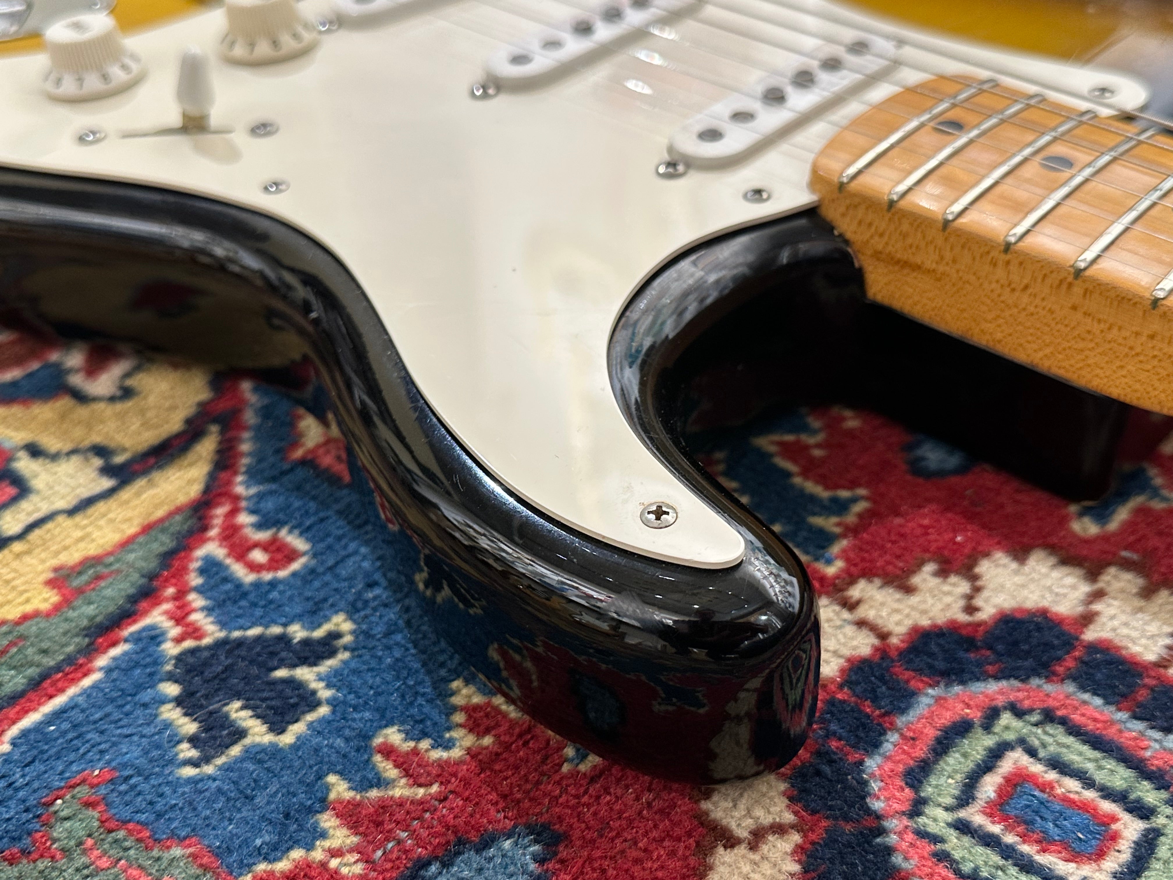 Close-up of a black electric guitar neck on a colorful patterned rug